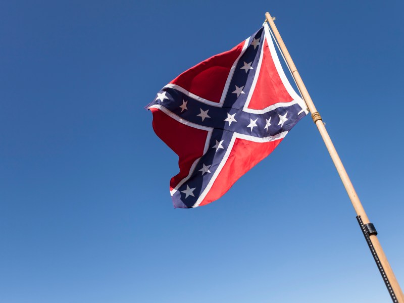 Confederate Flag on pole over blue sky.